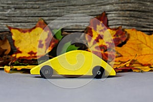 Yellow wooden toy car with cloorful leaves