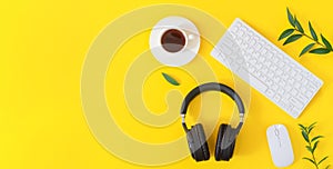 Yellow workplace with wireless headphones, keyboard, mouse, cup of cofffe from above
