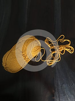 Yellow yarn unraveling on dark wood table