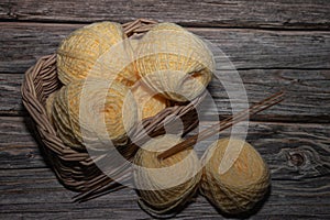 yellow yarns in basket and wooden crochet needle on wooden textured background