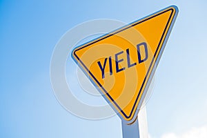 A yellow yield sign against a blue sky background