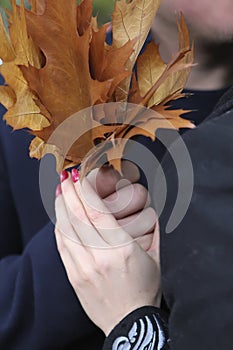 Yellowed leaves in the form of a bouquet in the hands of a couple of man and woman in autumn against a background of dark blue out