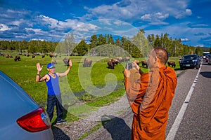 YELLOWSTONE, MONTANA, USA MAY 24, 2018: Unidentified monk taking pictures with a camera to a tourist, with a herd of