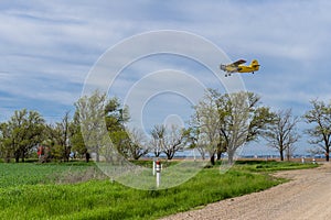 Yelow crop duster airplane flies over the farm field and road