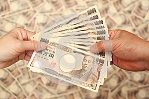 YEN - Japanese money: Hands holding paying / receiving 100,000 yen banknote.