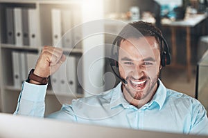 Yes Another issue resolved. a young call centre agent sitting alone in his office and celebrating a success while using