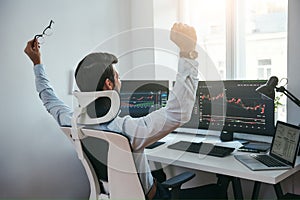 Yes Back view of stock trader with raised hands looking at multiple computer screens with data and charts and feeling