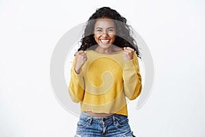 Yes deal mine. Successful african-american cute woman in yellow sweater, smiling happily, celebrating amazing news