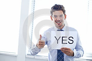 YES. a handsome young businessman holding a yes sign and giving the thumbs up.