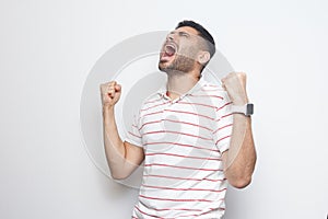 Yes I win. Portrait of happy screaming handsome bearded young man in striped t-shirt standing with fists and rejoicing or