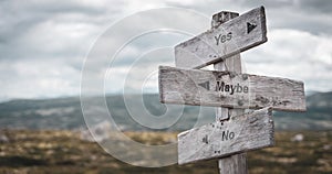 yes maybe no text engraved on wooden signpost outdoors in nature.