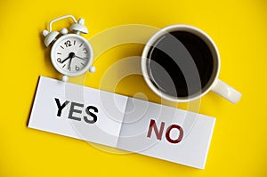 Yes and no text on notepad with alarm clock and coffee cup on yellow background. Decision making concept.