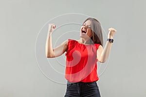 Yes! Portrait of happy beautiful brunette young woman in red shirt standing and celebrating her victory with happiness and