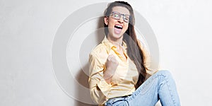 YES. Portrait of young excited and screaming girl over white studio background. Wearing blue jeans, glasses and yellow