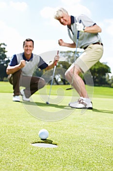 Yes. Two excited men on the green during a round of golf watching the ball rolling into the hole.