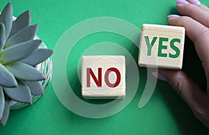 Yes vs No symbol. Businessman hand is making a choice between YES and No symbol. Beautiful green background with succulent plant.