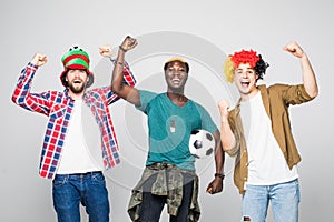 Yes. Winners. Three cheerful young men are standing and gesturing for the victory on white background in casual outfit and jeans.