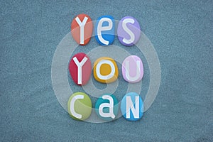 Yes, you can, creative and motivational slogan composed with multi colored stone letters over green sand
