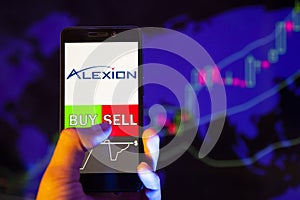 Company logo Alexion Pharmaceuticals, Inc ALXN on smartphone screen, hand of trader holding mobile phone showing BUY or SELL on