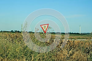 Yield sign on the road. Red traffic sign Give Way with moving motorcycle and wind turbines on background