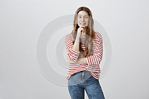 Yikes, mom saw broken vase. Studio shot of pretty embarrassed teenage girl holding hand on chin and grimacing with