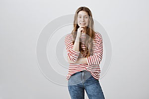 Yikes, mom saw broken vase. Studio shot of pretty embarrassed teenage girl holding hand on chin and grimacing with photo