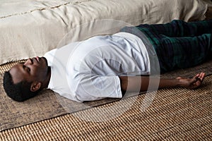 Yoga. African young man meditating on a floor and lying in Shavasana pose.