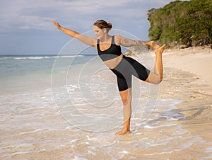 Yoga on the beach. Young woman practicing yoga, preparing for Natarajasana, Lord of the Dance Pose. Balancing, back bending asana