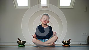 yoga for children, cute boy concentrated on meditation sits in lotus position on karimat near tibetan musical bowls in a