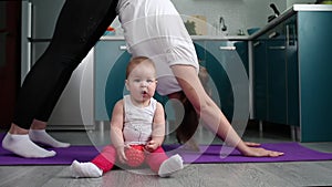 Yoga with children. A young mother is doing yoga, and the baby is sitting near the mat with a toy in his hands. The concept of hom