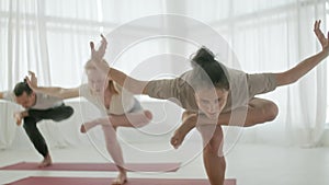 Yoga Class Group of Three Women and Man Exercising Healthy Lifestyle in In Bright Studio. People balancing on one leg in