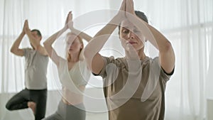 Yoga Class Group of Three Women and Man Exercising Healthy Lifestyle in In Bright Studio. People balancing on one leg in