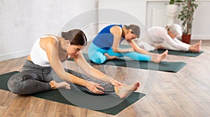 Yoga class of relaxed sports women performing Head to Knee Forward Bend Pose, or Janu Sirsasana after practicing