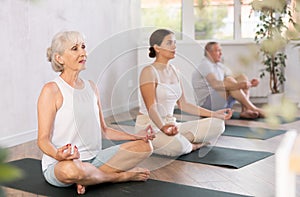 In yoga class senior lady performs lotus pose-Padmasana-Siddhasana with friends