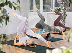Yoga class of sporty women in activewear performing Halasana or Plow Pose on mats during workout in cozy yoga studio