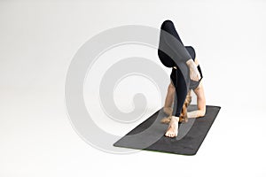 Yoga class in white studio, advanced pose. Young woman in black sportswear