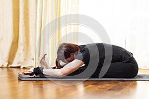Yoga Concept. Caucasian Woman Practicing Yoga Exercise Indoors At Bright Afternoon. Sitting in Pashchimottasana Pose