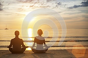 Yoga couple meditating on the coast during the amazing sunset.