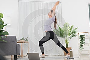 Yoga exercise concept, Young Asian woman watching yoga tutorial online to doing warrior pose on mat