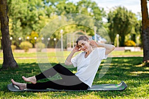 Yoga and fitness. A young woman in sports clothes, sitting performs an exercise, doing sports in the Park on the grass