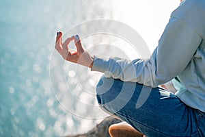 yoga, gesture and healthy lifestyle concept - hand of meditating yogi woman showing gyan mudra over sea sunset