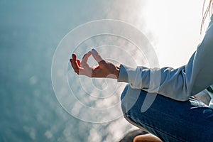 yoga, gesture and healthy lifestyle concept - hand of meditating yogi woman showing gyan mudra over sea sunset