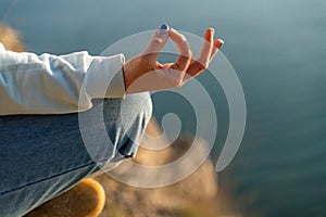 yoga, gesture and healthy lifestyle concept - hand of meditating yogi woman showing gyan mudra over sea sunset