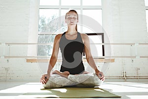 Yoga girl performs asana. Happy young woman practicing yoga in white sunny gym early morking