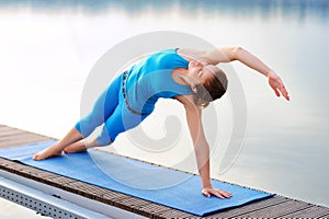 Yoga girl practicing side plank positing at the river bank in th