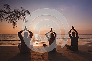 yoga group on the beach, silhouettes of people meditating in lotus position at sunset