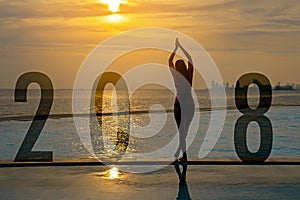 Yoga Happy new year card 2018. Silhouette woman practicing yoga on swimming pool standing as part of Number 2018 near the beach at