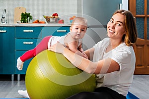 Yoga at home. Portrait of a young mother leaning on a fit ball and posing with your baby. The concept of fitness with children at