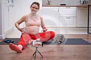 Yoga at home during pregnancy and online training course. Pregnant woman on workout shows exercises on video from the Internet via