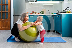 Yoga at home. A smiling young mother leaning on a fit ball and talking with her baby. The concept of fitness with children at home